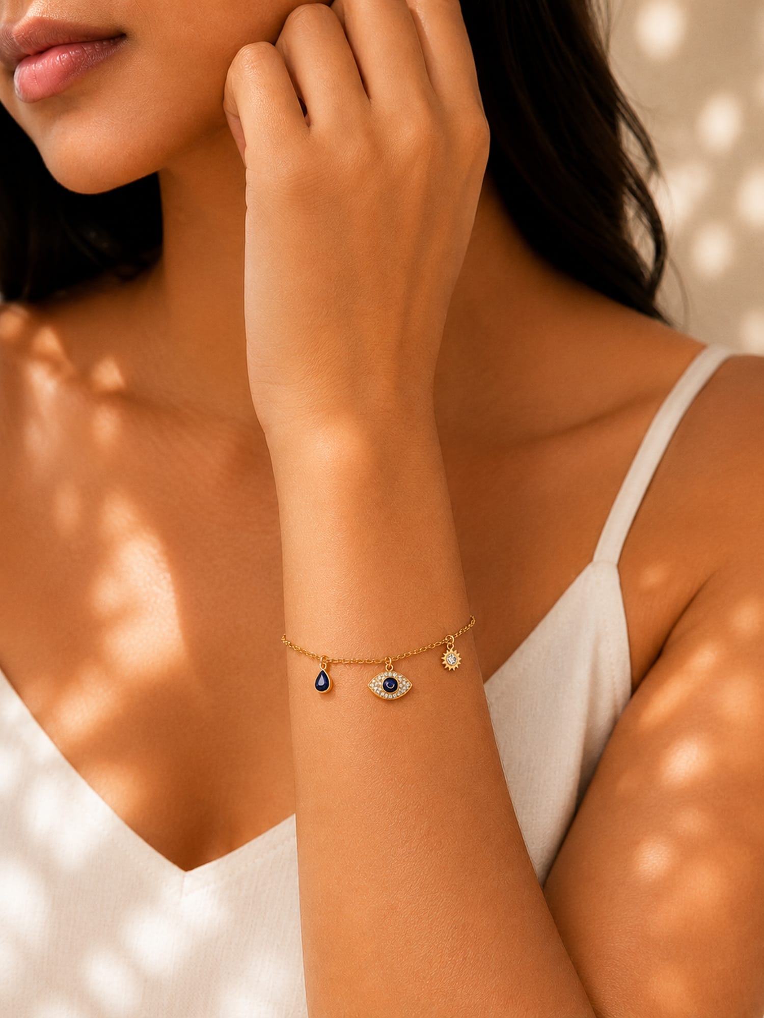A gold charm bracelet with an evil eye pendant and a small round charm, worn on a model's wrist.