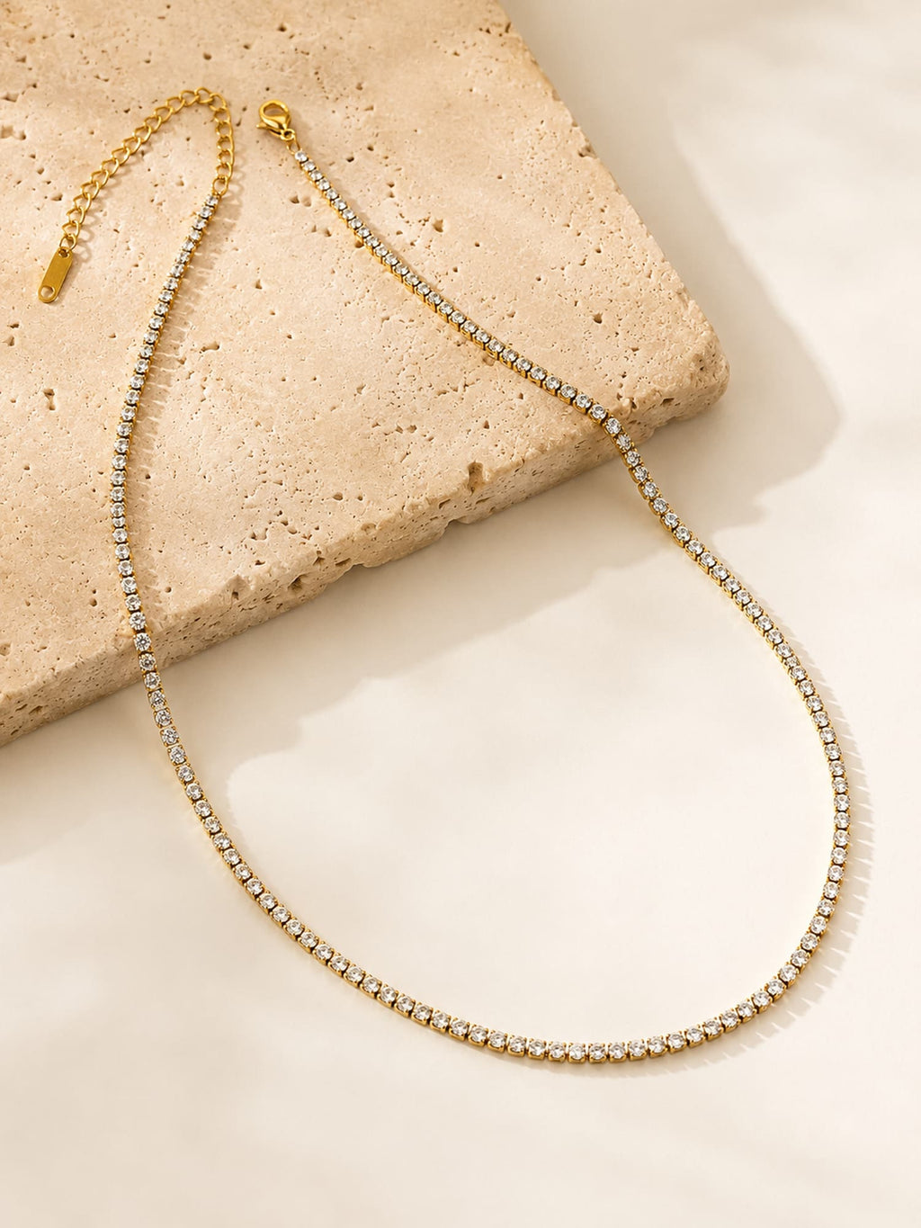 Minimalist CZ tennis necklace displayed on a textured stone surface showcasing its elegant gold-plated finish and sparkling white stones.