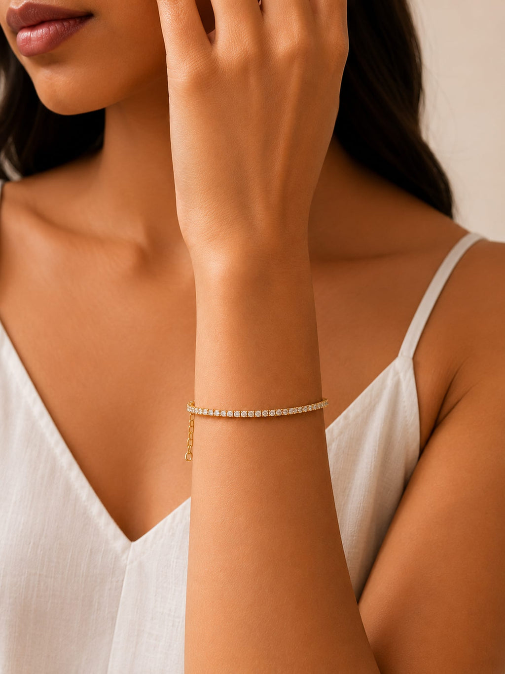 A delicate gold bracelet with a row of small clear stones worn on a woman's wrist, shown in a close-up lifestyle shot.