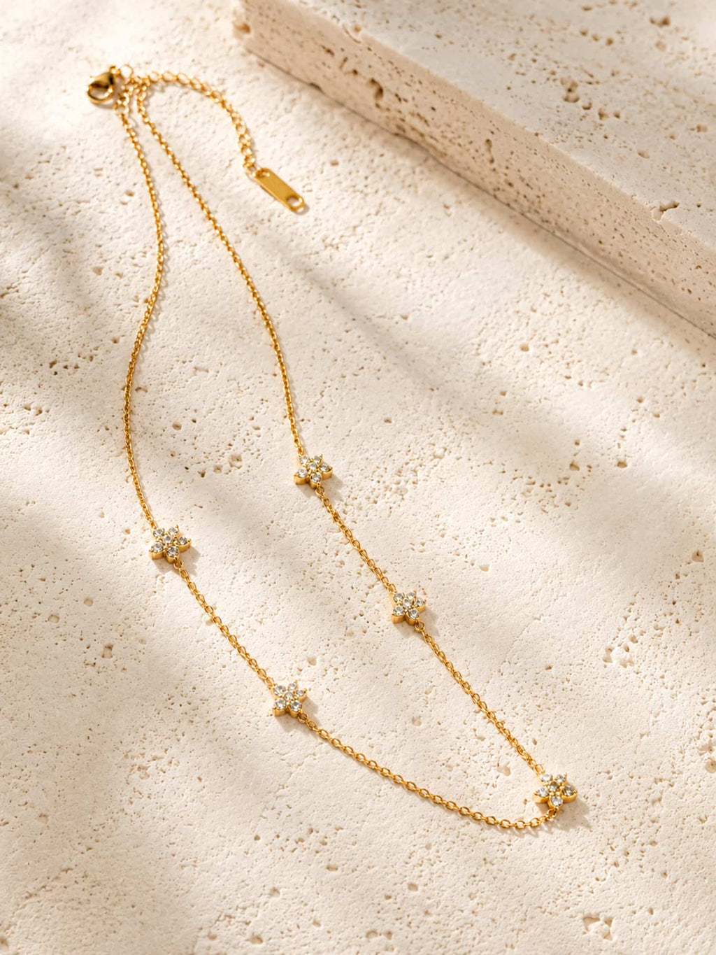 Minimalist floral CZ station necklace displayed on a textured stone surface highlighting its elegant gold finish and delicate flower details.