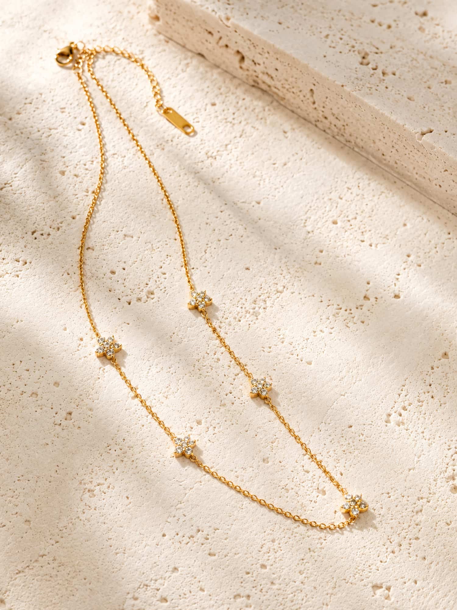 Minimalist floral CZ station necklace displayed on a textured stone surface highlighting its elegant gold finish and delicate flower details.