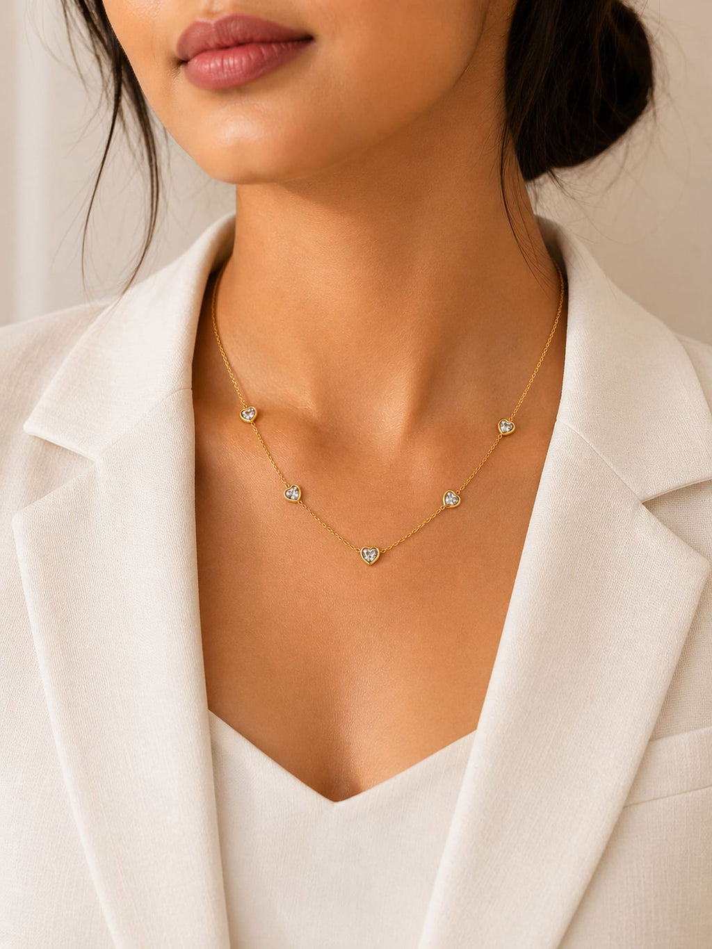 A close-up of a model wearing a delicate gold necklace with five small, clear, diamond-like starburst charms, styled with a white blazer.
