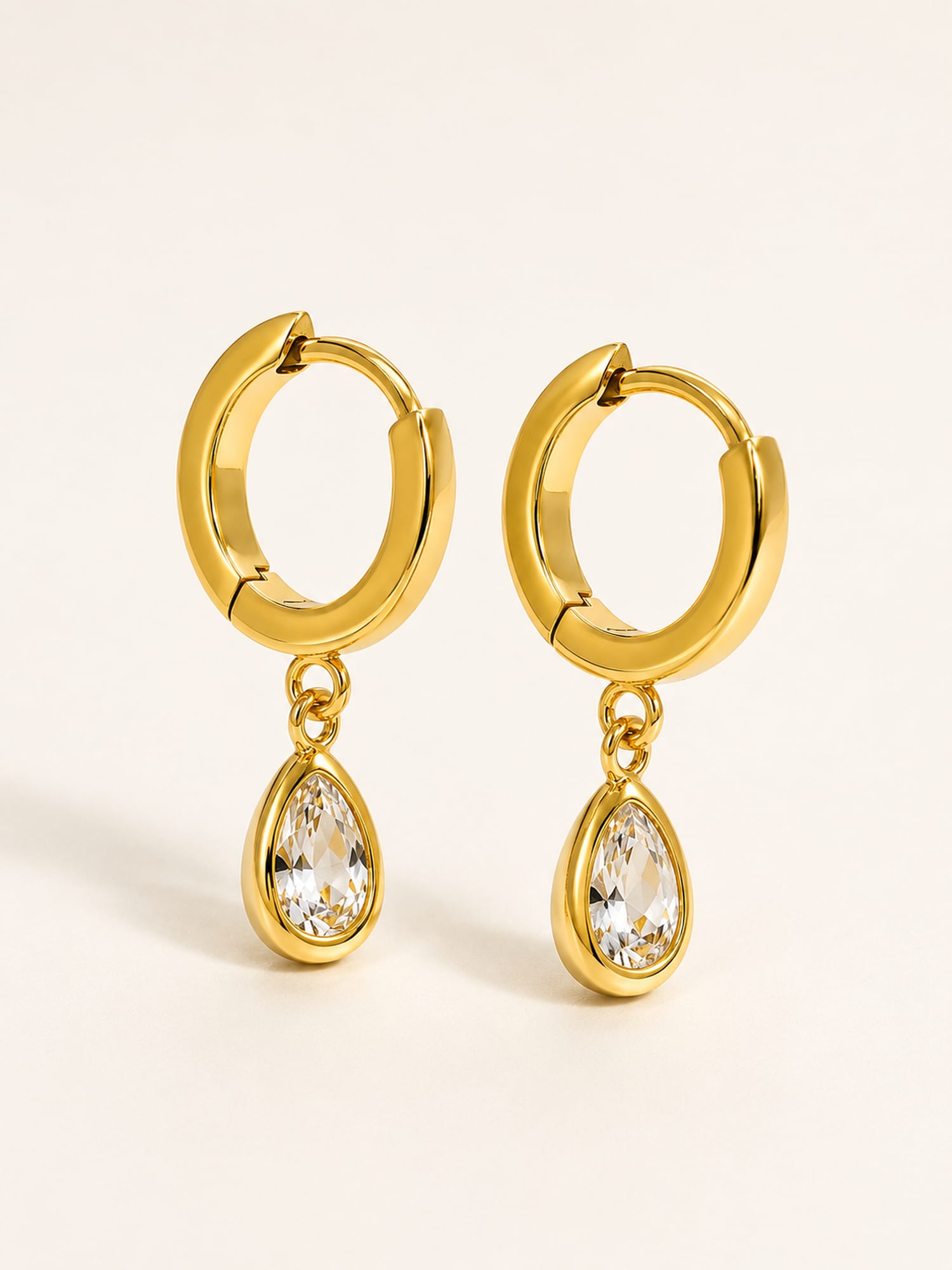 Gold huggie earrings featuring teardrop white cubic zirconia drops in a timeless minimalist design.